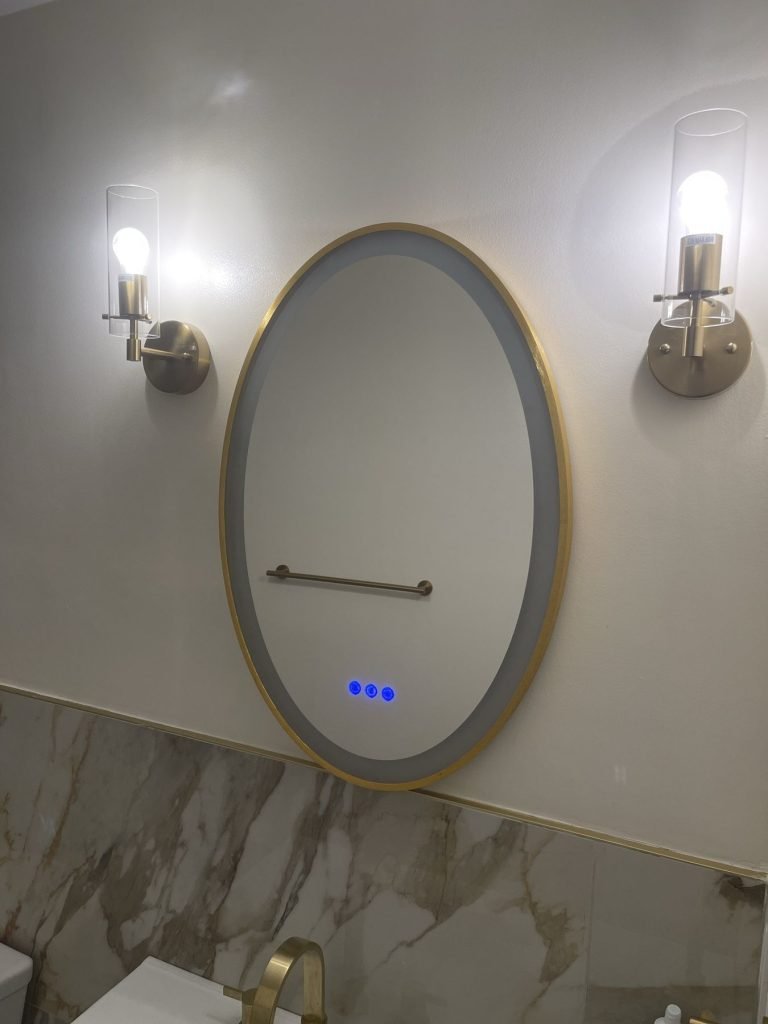 Oval backlit mirror between brass wall sconces