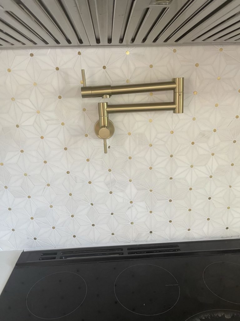 Brass pot filler over a marble mosaic backsplash