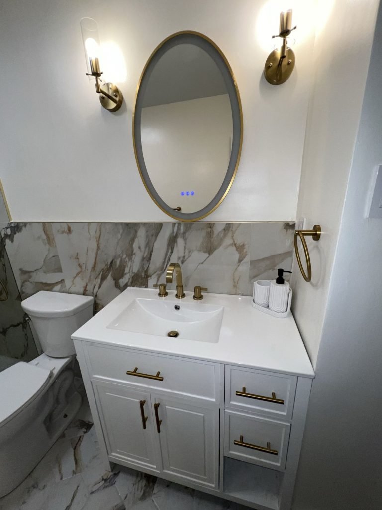White vanity with brass fixtures and oval mirror