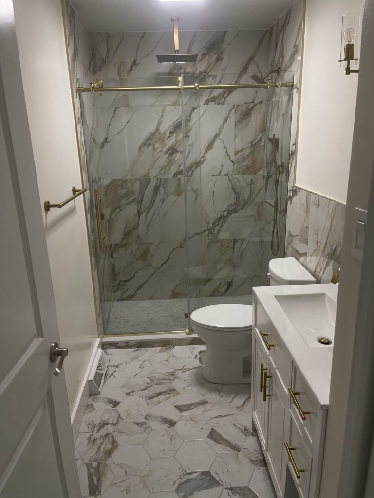 Bathroom remodel with marble-look porcelain shower and brass frameless glass door