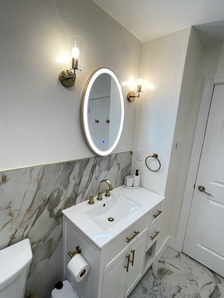 White vanity with oval LED mirror and brass sconces