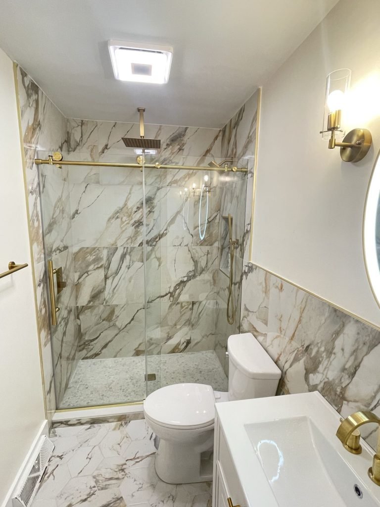Walk-in shower with brass glass door hardware and marble-look tile