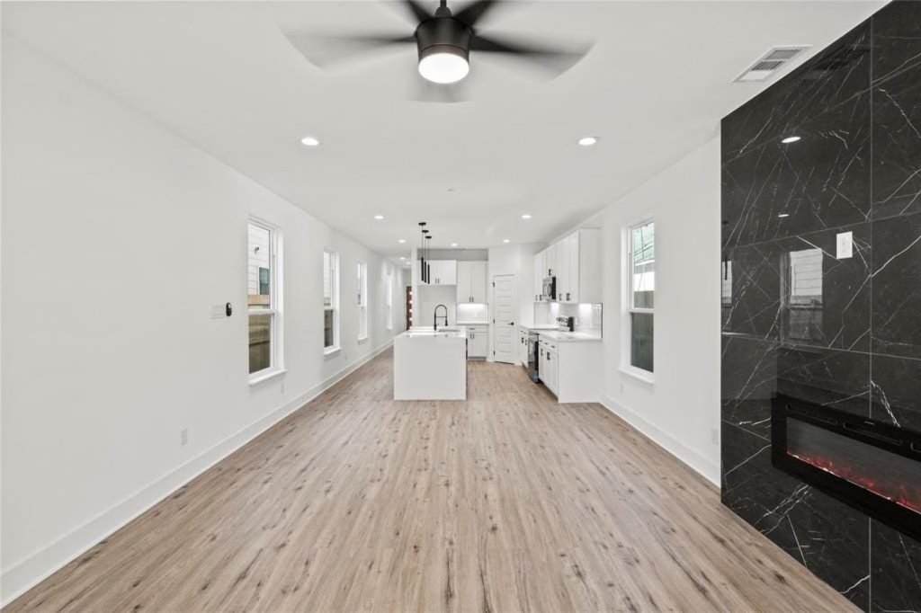 Long rowhouse living room with black marble-look fireplace wall and new plank flooring
